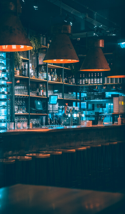 A long bar with bar stools and low lights. The bar is illuminated in colours of blue and orange.