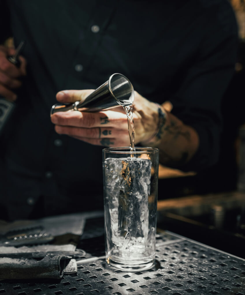 A close up shot of a bartender pouring a shot of clear liquid into a glass of ice.